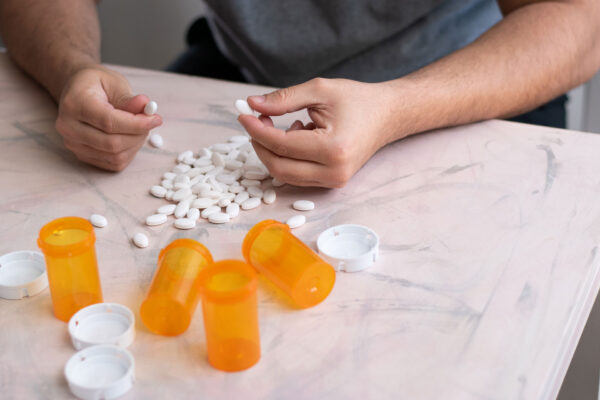 Addicted man taking pills with hands from a lot of medicine drugs on table